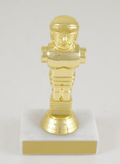 A shiny gold metallic figurine of a foosball figure mounted on a square white base with a gold front panel, photographed against a plain light background.