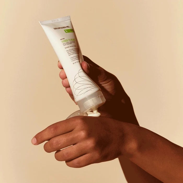 A close-up of hands applying Goldfaden MD Hands to Heart cream, with the product tube held in one hand.