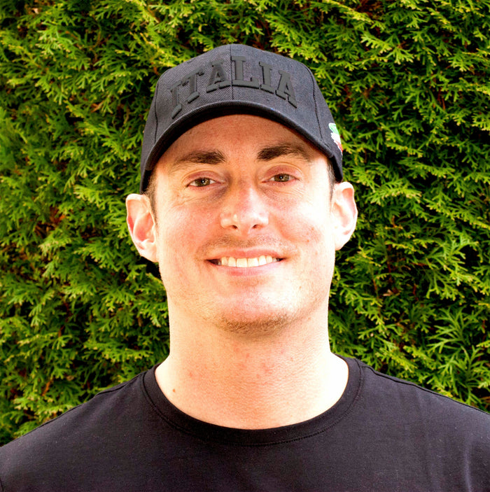 Black baseball cap featuring bold, all-caps “ITALIA” embroidery across the front in gray thread. A brushstroke design in green, white, and red—representing the Italian flag—adorns the side, making this cap a stylish tribute to Italian pride and heritage on man's head