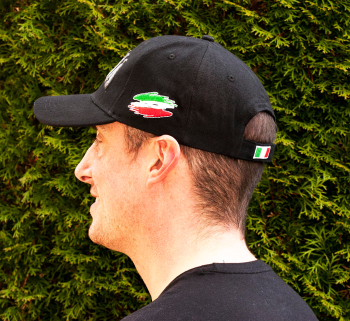 Black baseball cap featuring bold, all-caps “ITALIA” embroidery across the front in gray thread. A brushstroke design in green, white, and red—representing the Italian flag—adorns the side, making this cap a stylish tribute to Italian pride and heritage. Side profile view of the cap