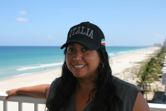Woman wearing a 'ITALIA' cap with a beach and ocean in the background