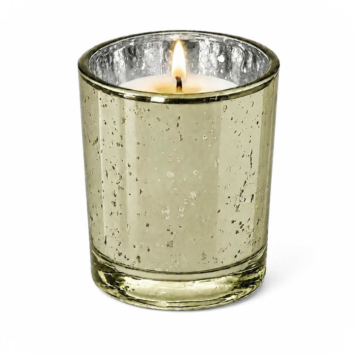 A single lit candle burning inside a Metallic Gold Mercury Votive Holder on a white surface
