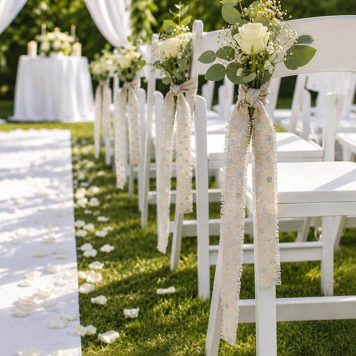 White chairs lining a wedding aisle decorated with linen ribbons and flowers