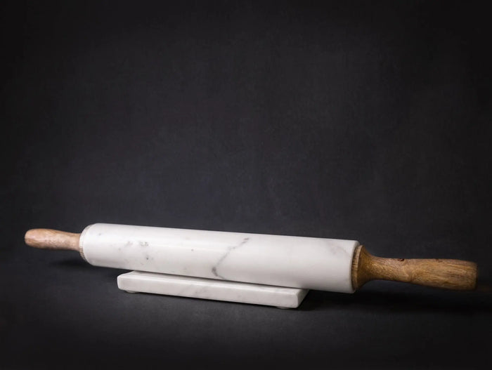 A professional 18-inch rolling pin featuring a white marble center and tapered mango wood handles, resting on a matching marble and wood storage cradle.