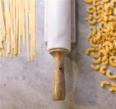 A professional 18-inch rolling pin featuring a white marble center and tapered mango wood handles, resting on a matching marble and wood storage cradle.