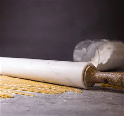 A professional 18-inch rolling pin featuring a white marble center and tapered mango wood handles, resting on a matching marble and wood storage cradle.